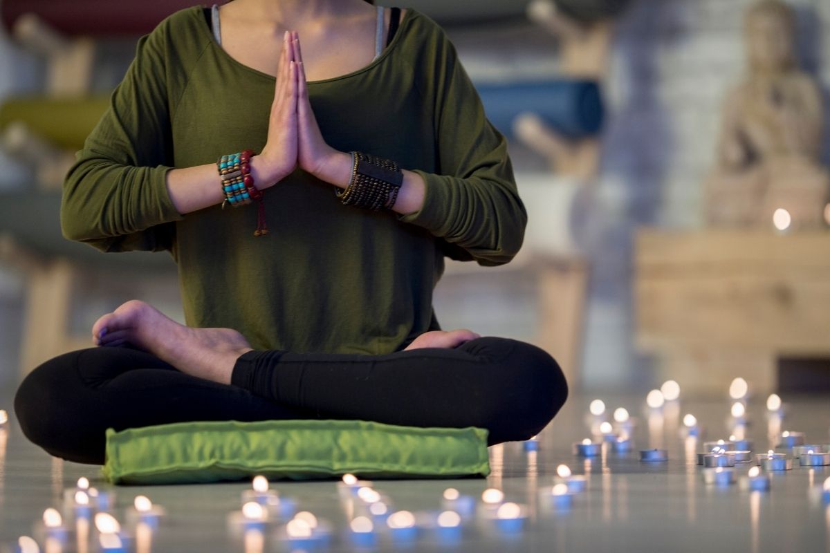 A woman meditating with pillow and candles.